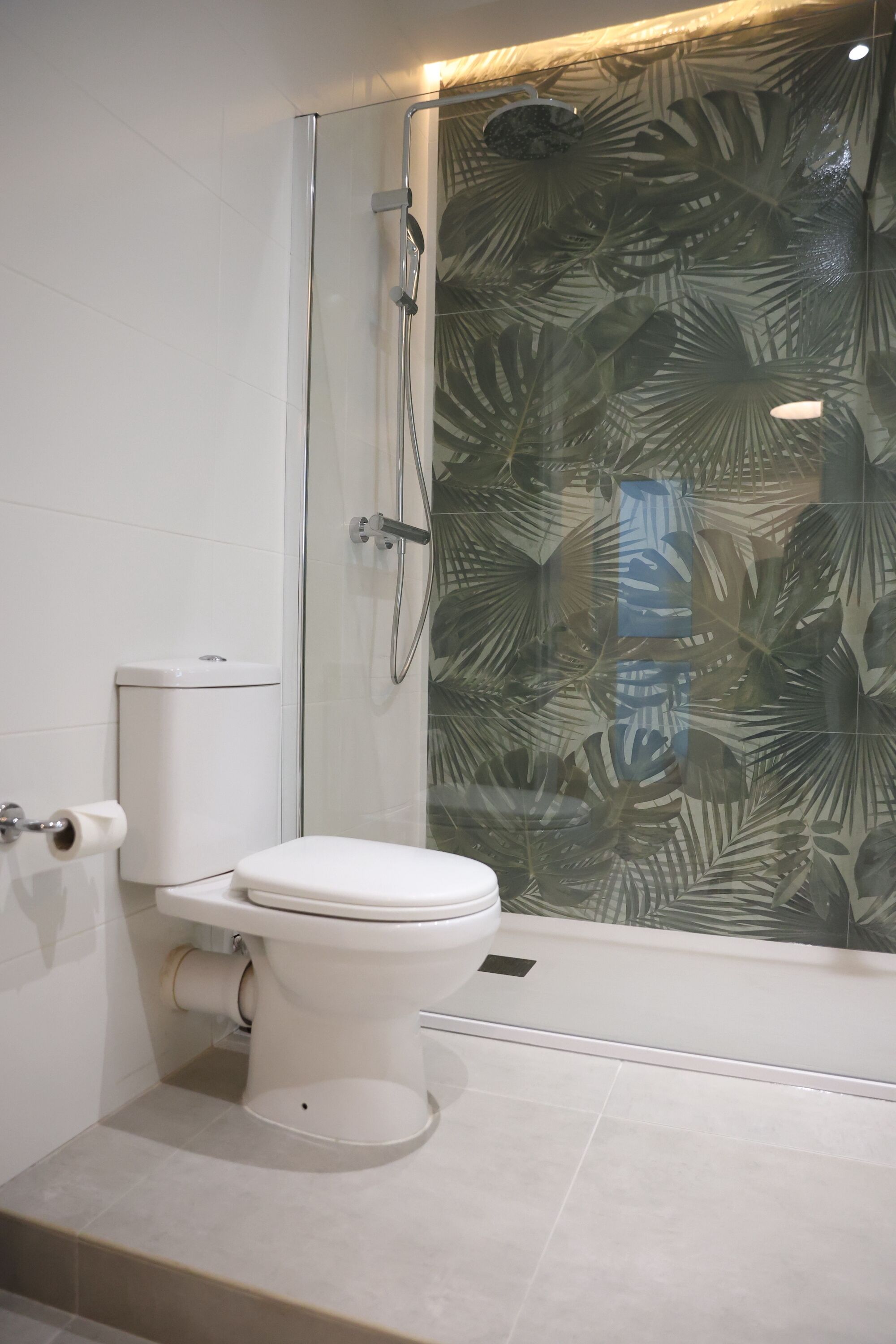 A bathroom with a toilet, a glass shower enclosure, and a toilet paper holder.