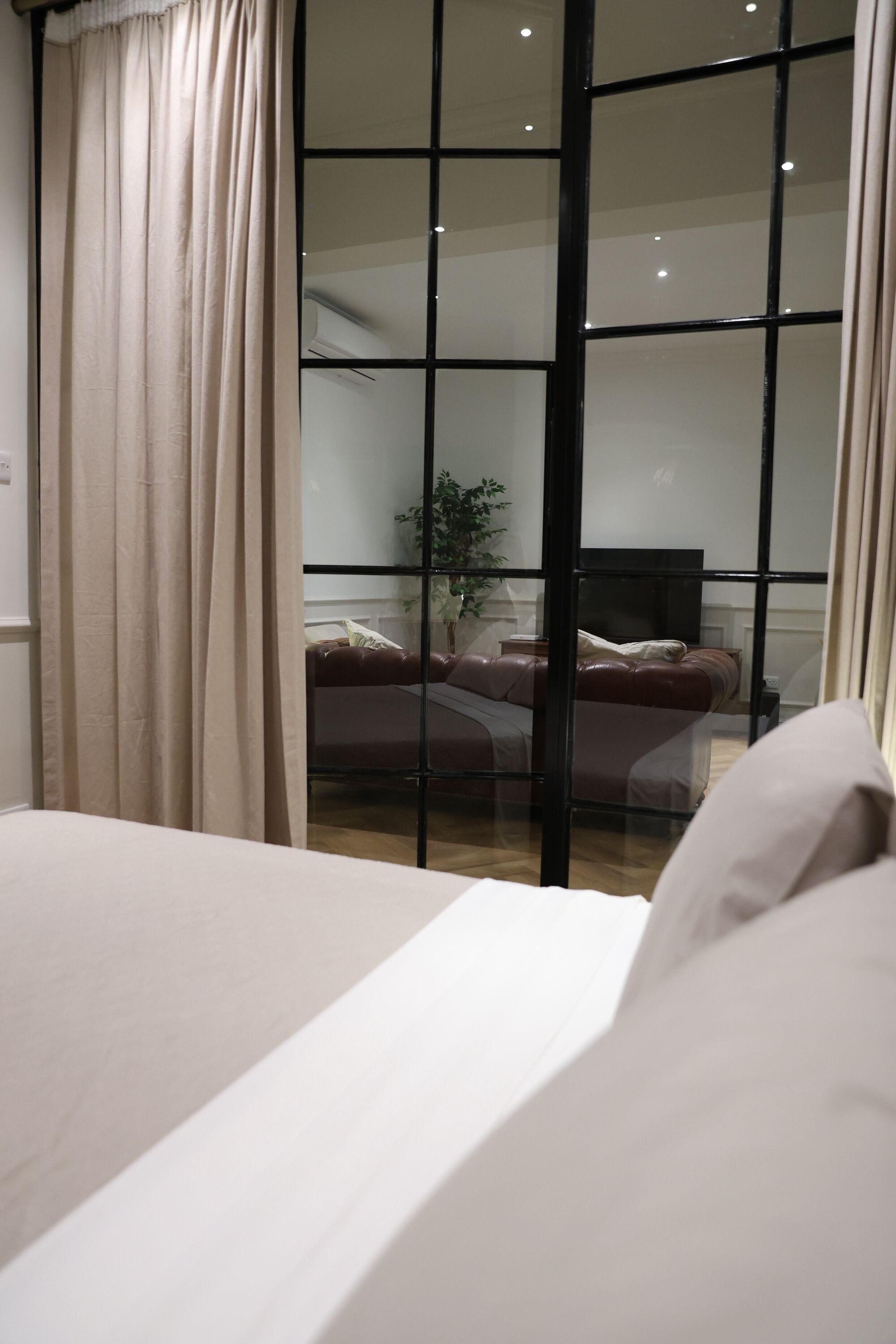 Une chambre avec une grande fenêtre, un lit et une vue sur un espace de vie comprenant un canapé et un téléviseur.