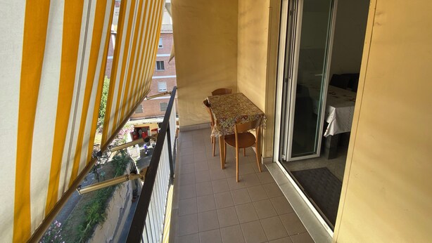 A balcony with yellow-striped curtains, a table with chairs, and a sliding glass door leading to a room.