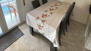 A dining area with a table covered in a floral tablecloth, four chairs, and a view of a balcony through a door with a striped curtain.
