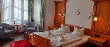 A hotel room with a wooden bed, two matching chairs, a small table, and a red rug.