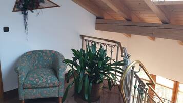 A room with a floral-patterned armchair, a potted plant, and a staircase with a metal railing.