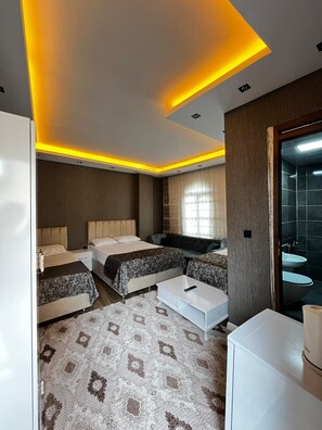 A modern hotel room with two beds, a sofa, a coffee table, and a bathroom with a sink and mirror. - Derin Park Hotel (Sanliurfa)