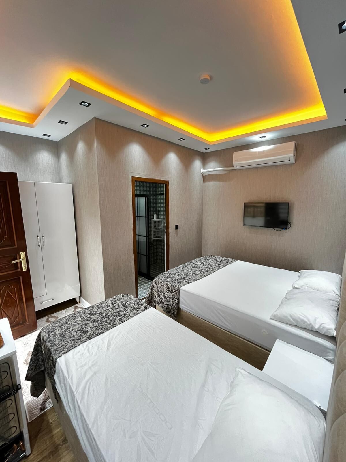 Una habitación de hotel con dos camas, un armario, un televisor y un equipo de aire acondicionado.