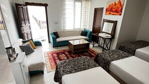 Une chambre d’hôtel avec un canapé, deux lits simples, une petite table, un bureau et une fenêtre avec des rideaux.