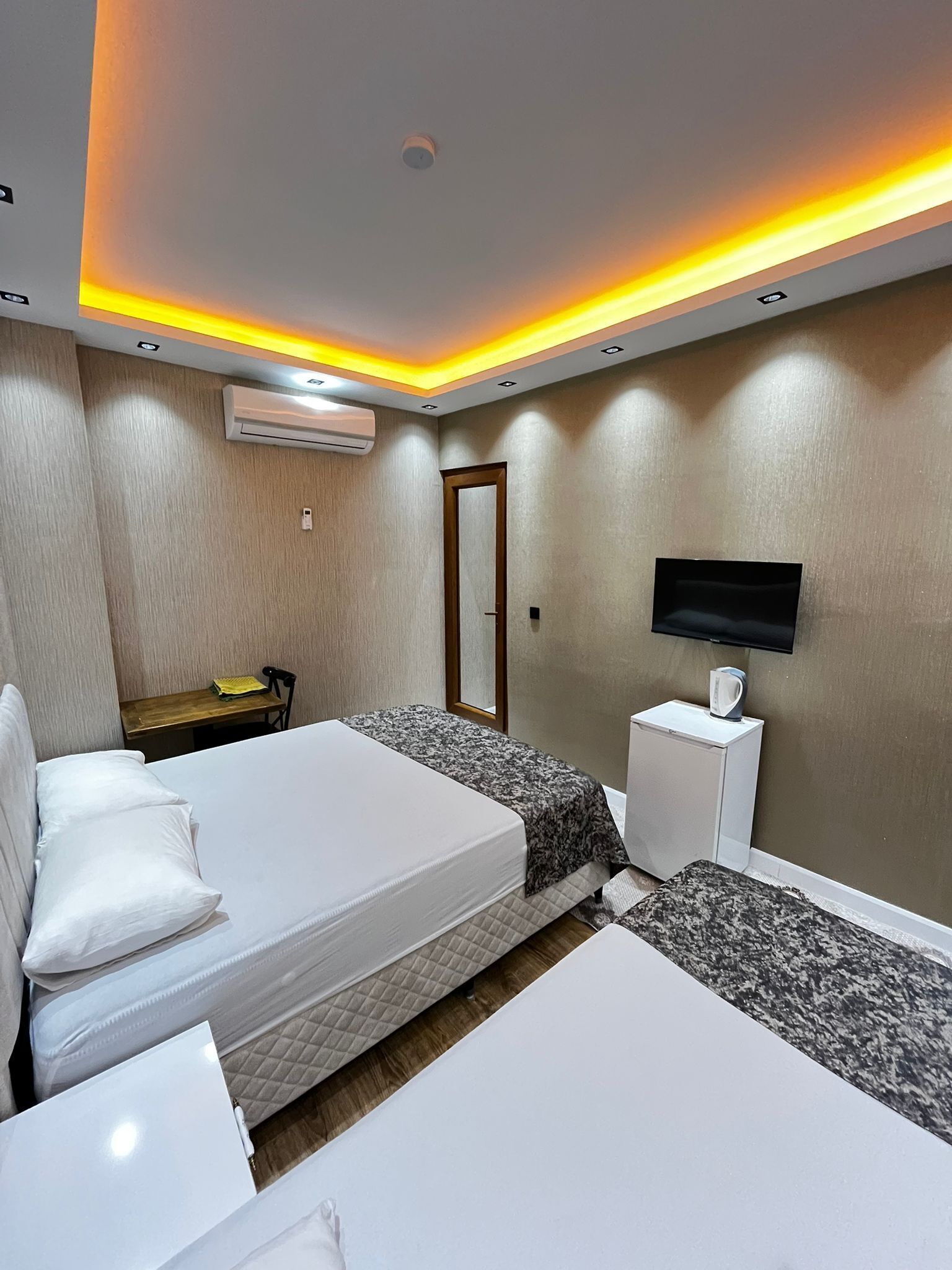 A hotel room with two beds, a TV, a desk, and an air conditioning unit.