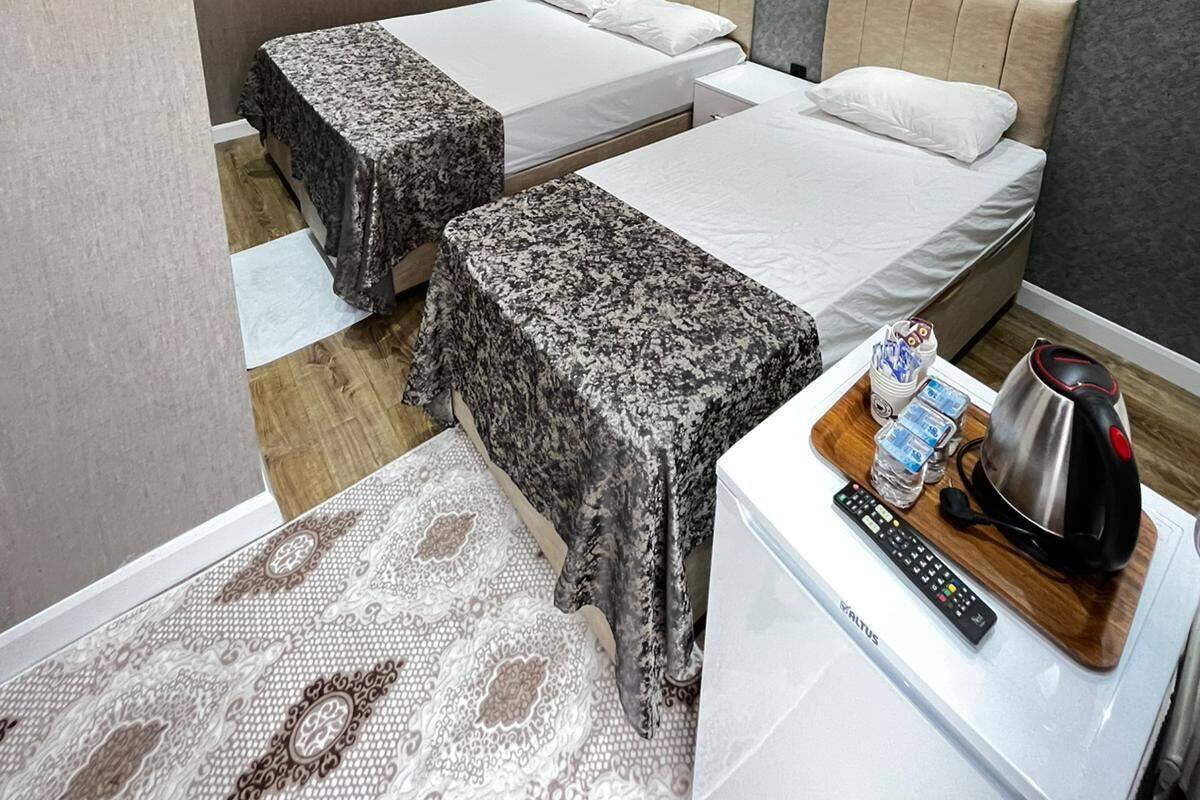A hotel room with two beds, a flat-screen TV, an air conditioning unit, a coffee maker, and a remote control on a bedside table.