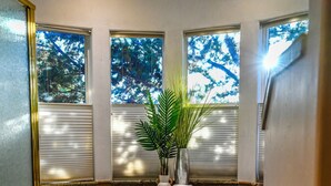 Un baño con bañera, una planta en maceta y vistas a árboles a través de las ventanas.