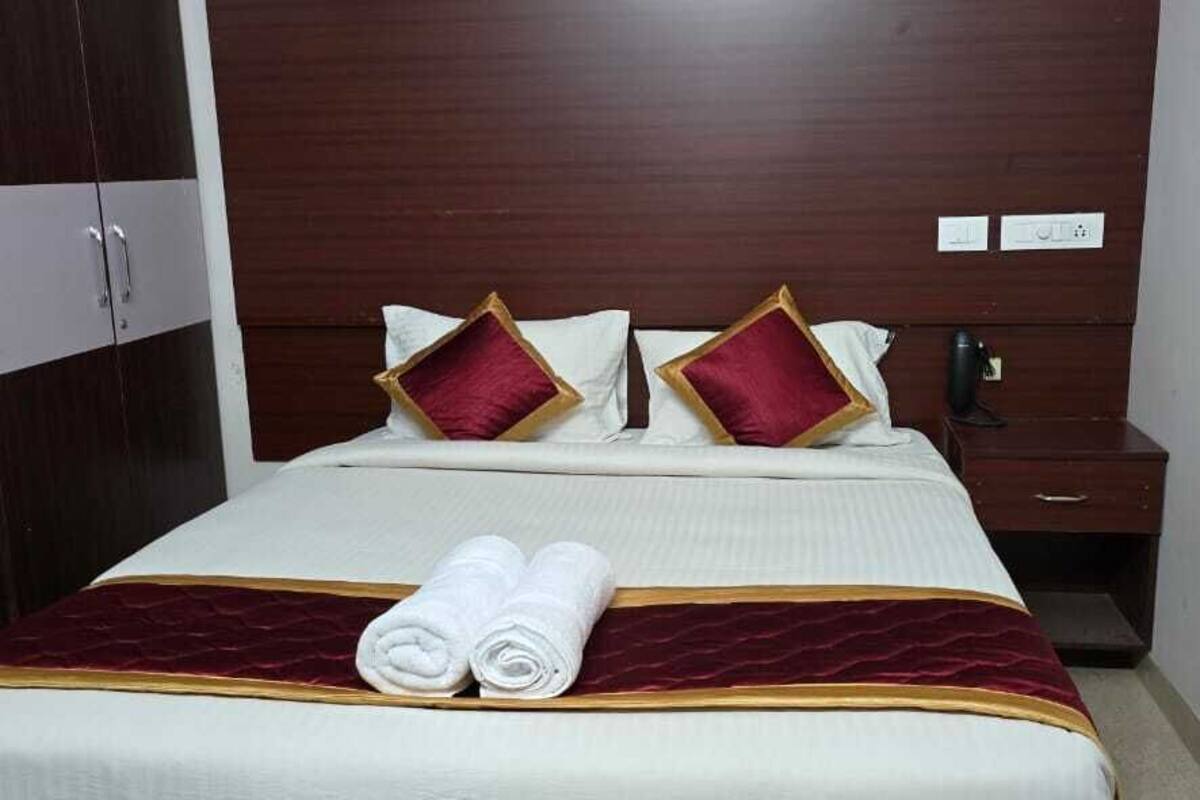 A hotel room with a neatly made bed, a wooden wardrobe, and a bedside table with a lamp.