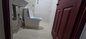 A bathroom with a toilet, shower, and a door. - PPH Living Arvind Inn (Coimbatore)