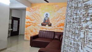 A room with a brown leather sofa, a mural of a meditating figure on the wall, and a patterned curtain. - PPH Living Arvind Inn (Coimbatore)