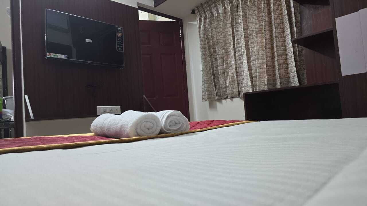 Una habitación de hotel con una cama, un televisor fijado en la pared y una ventana con cortinas.