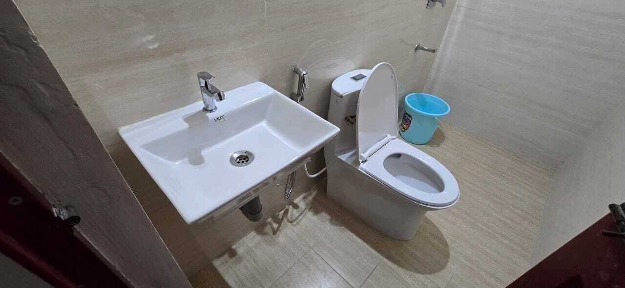 Une salle de bain avec un lavabo blanc, des toilettes et un seau bleu.