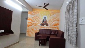 A room with a brown sofa, a small table, a ceiling fan, and a mural of a meditating figure on the wall. - PPH Living Arvind Inn (Coimbatore)