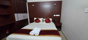 A hotel room with a large bed, a wooden wardrobe, and a nightstand with a lamp. - PPH Living Arvind Inn (Coimbatore)