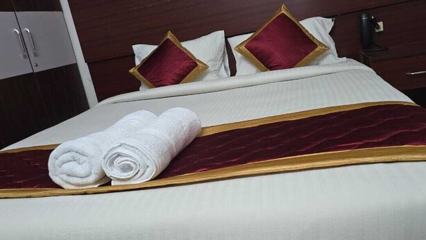 A neatly made bed with a white and gold bedspread, two rolled white towels, and red and gold pillows. - PPH Living Arvind Inn (Coimbatore)