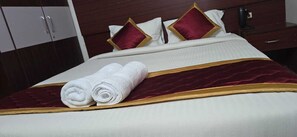 Un letto rifatto con cura, con copripiumino bianco e dorato, due asciugamani bianchi arrotolati e cuscini rossi e dorati.