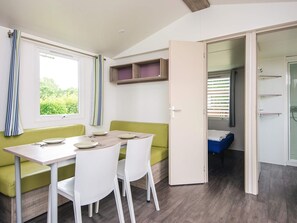 Une pièce de taille modeste comprenant une table et des chaises, un canapé vert, une armoire et un espace douche.