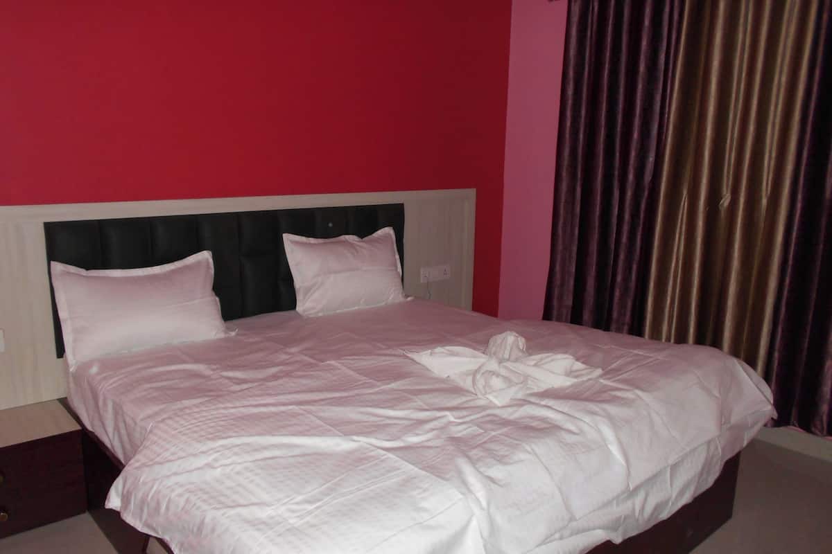 A neatly made bed with white linens and pillows, a dark headboard, and a red wall.