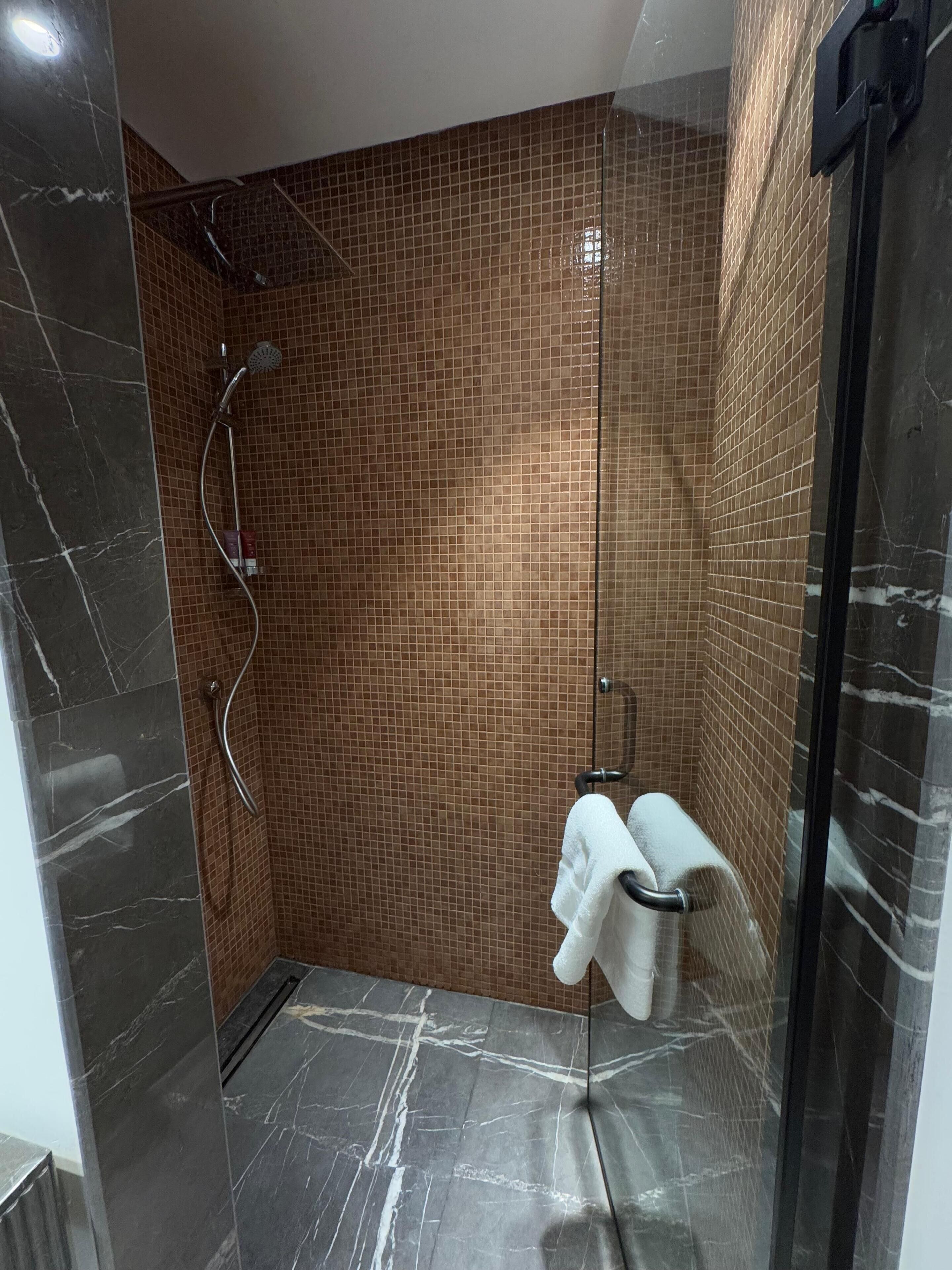 A modern bathroom with a glass shower enclosure, a tiled wall, and a marble floor.