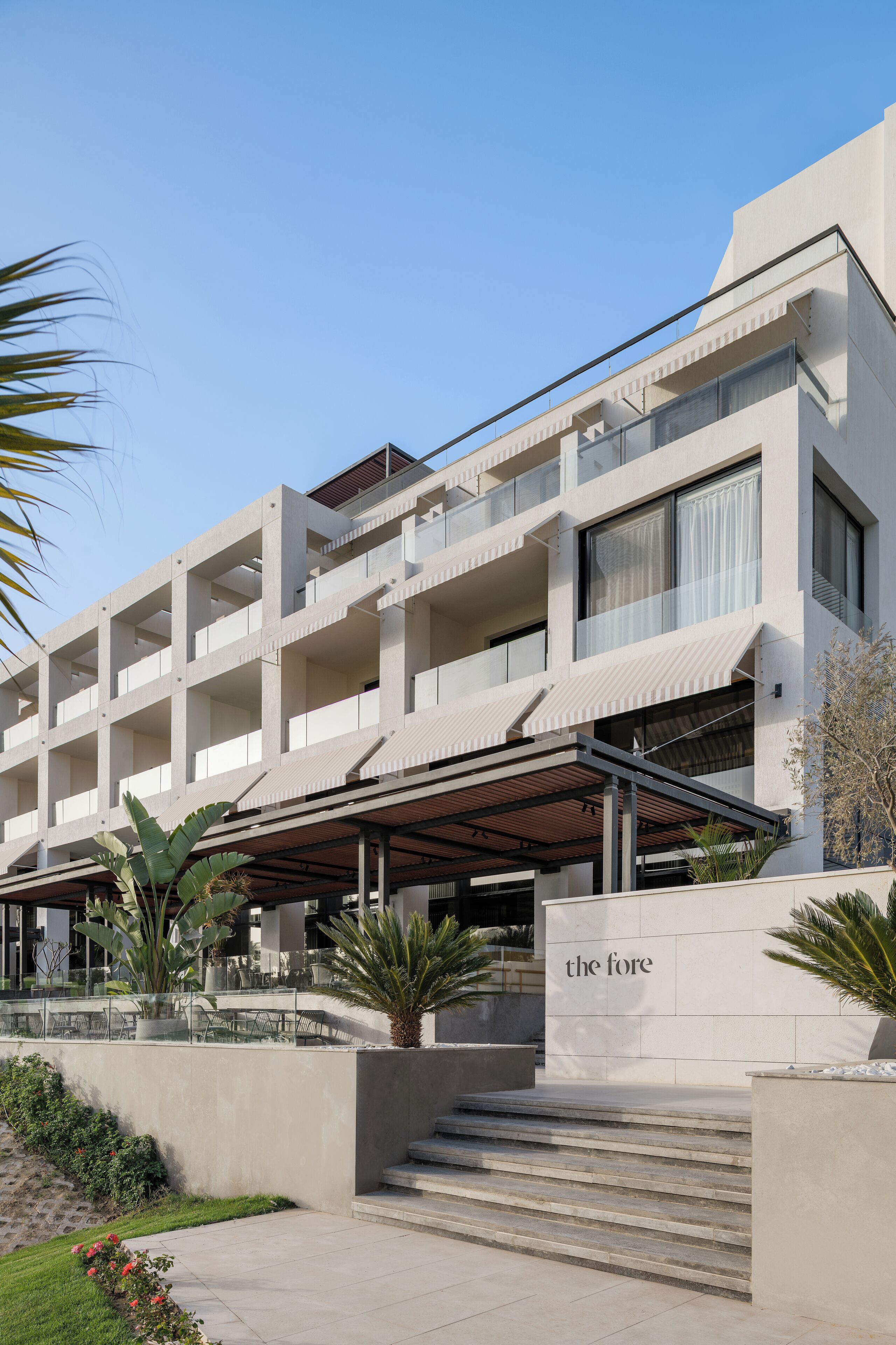 A multi-story hotel with a modern architectural design, featuring a covered entrance and a staircase leading to the entrance.