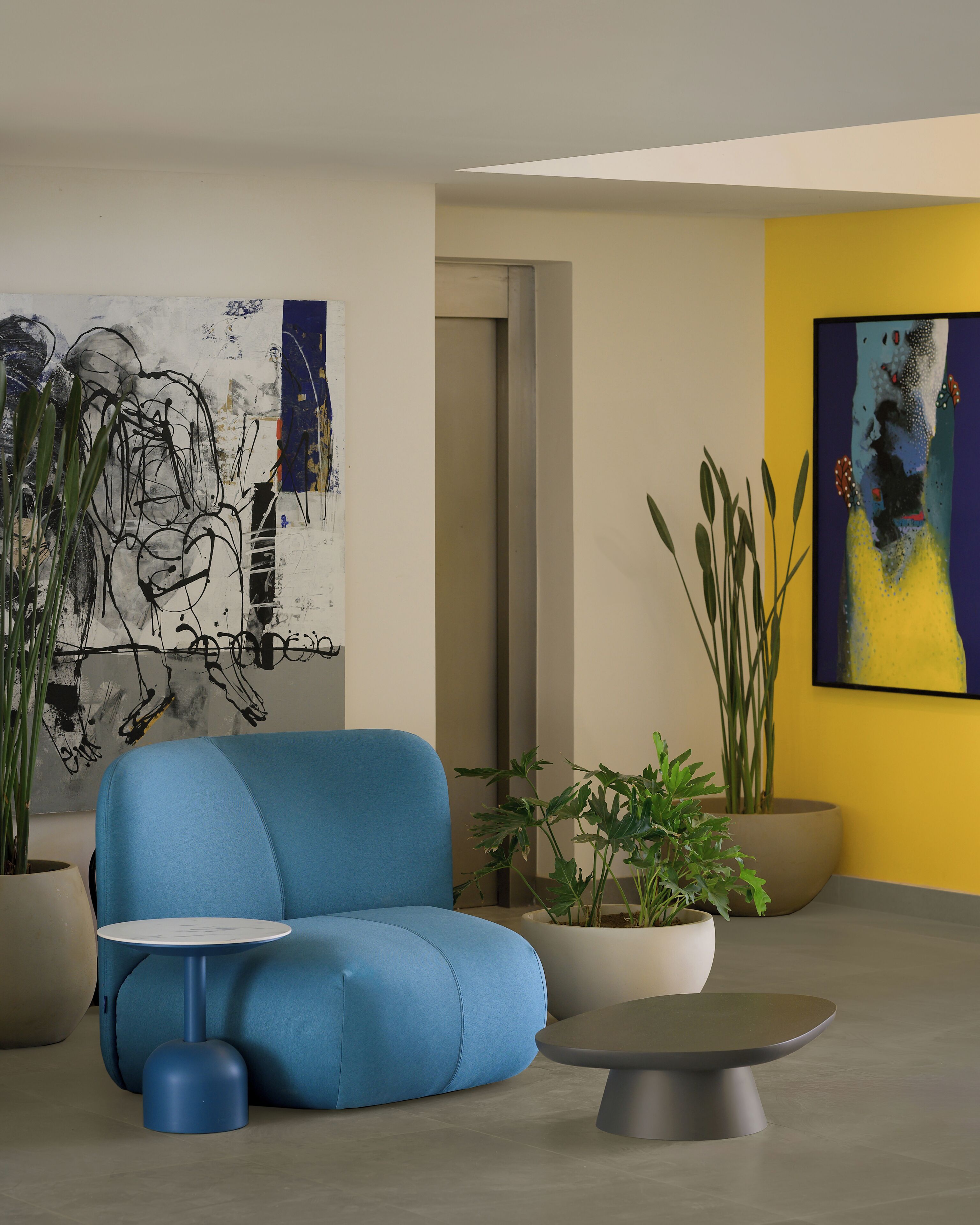 Een moderne woonkamer met een blauwe bank, een klein rond tafeltje en twee potplanten.