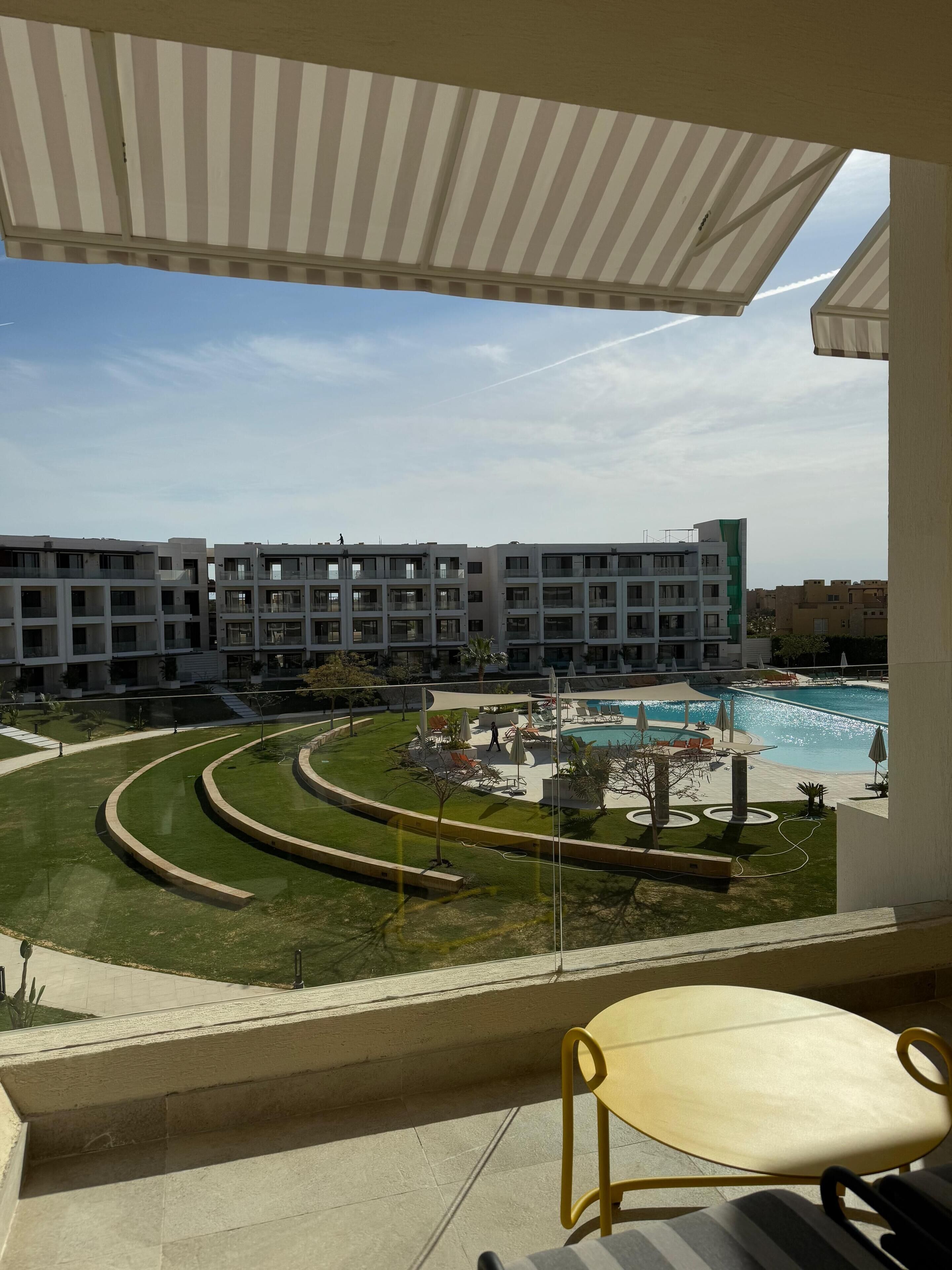Un balcon d’hôtel donnant sur une piscine et sur un immeuble à plusieurs étages en arrière-plan.