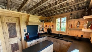 A rustic kitchen with wooden cabinets, a central island, and a window providing natural light. - Cosy Chalet With Balcony/terrace (Saanen)