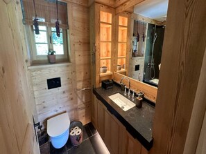 A compact wooden bathroom with a window, a sink, and a toilet.