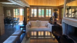 A cozy cabin interior with a wooden ceiling, a fireplace, a sofa, and a dining area with a table and chairs. - Cosy Chalet With Balcony/terrace (Saanen)