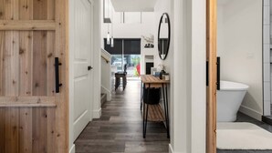 A hallway with a wooden door, a small table with chairs, a mirror, and a white bathtub. - Modern Mountain Townhouse at The Quarry (Whitefish)