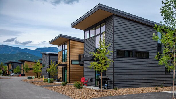 A modern residential building with a flat roof, large windows, and a small porch area. - Modern Mountain Townhouse at The Quarry (Whitefish)