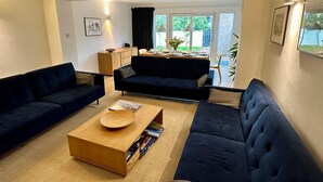 Una sala de estar moderna con sofás azul oscuro, una mesa de centro de madera y una zona de comedor con una mesa dispuesta para dos comensales.