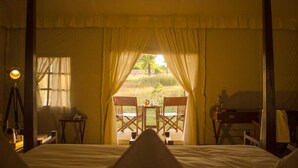 A room with a bed, two chairs, a small table, and a window with curtains. - Umaria Safari Camp -Kanha National Park  (Bichhiya)