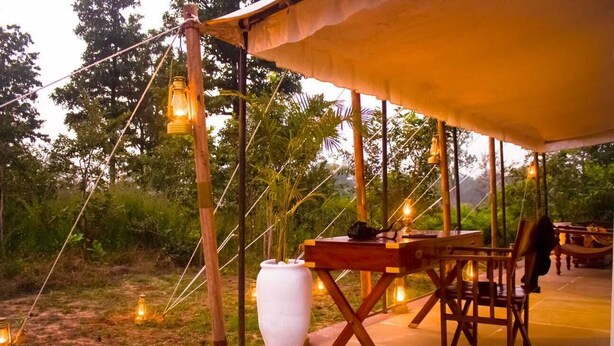 An outdoor seating area with a wooden table and chairs, surrounded by a canopy. - Umaria Safari Camp -Kanha National Park  (Bichhiya)