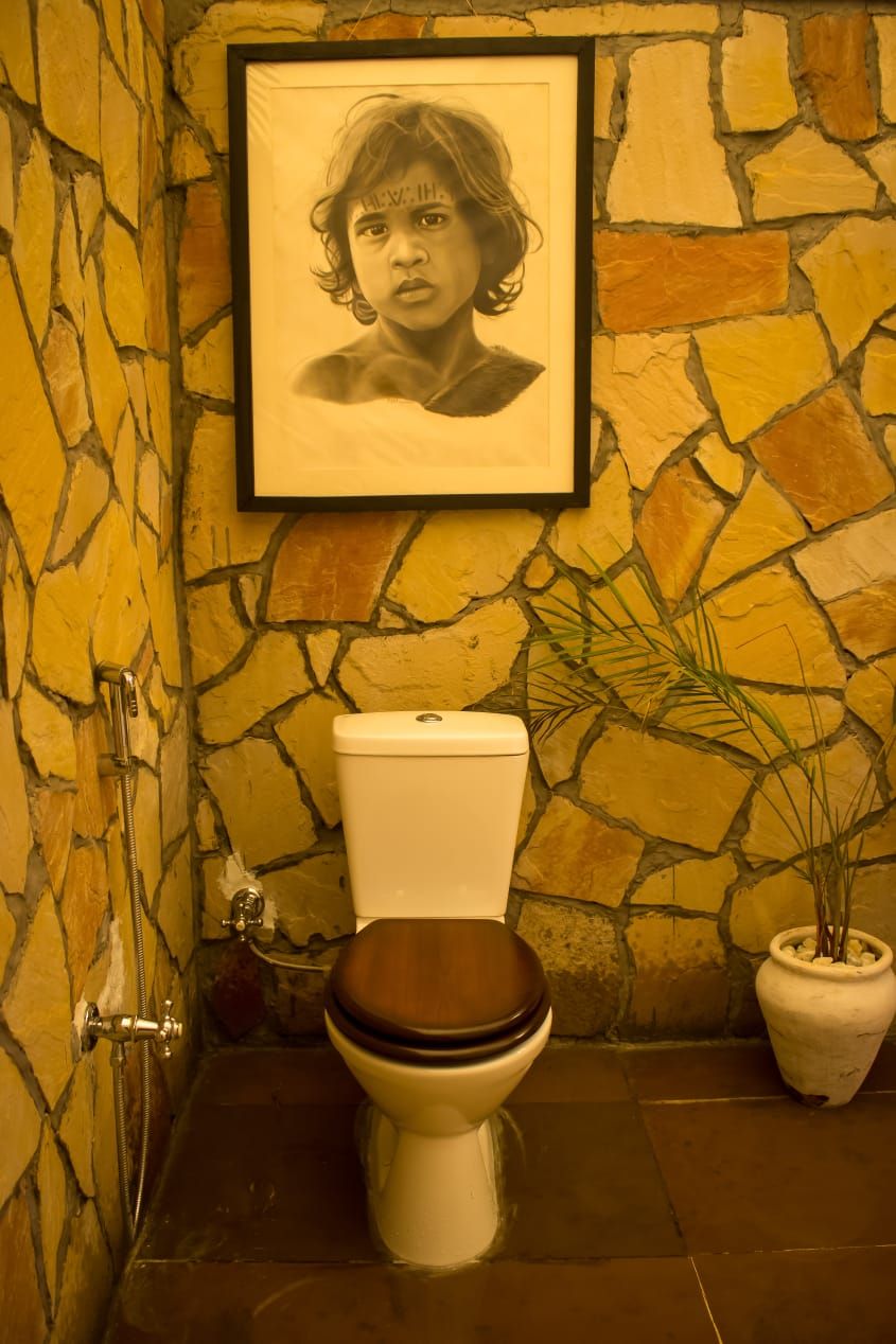 Une salle de bain avec un mur en pierre, un portrait encadré, des toilettes et une plante en pot.
