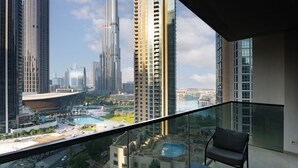 A high-rise building with a glass balcony overlooking a cityscape, including a large swimming pool and other buildings.