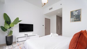 A modern hotel room with a large bed, a flat-screen TV, a potted plant, and a painting on the wall.