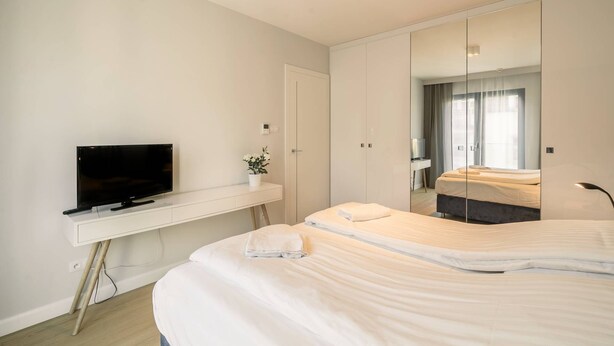 Un dormitorio con cama, televisor sobre un escritorio, armario y espejo.