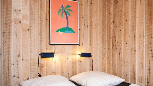 A room with wooden panel walls, a bed with white bedding, and a framed picture of a LEGO island. - 4 Person Holiday Park Home in Jelling (Jelling)