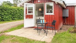 A small, red wooden building with a white door open, revealing a small kitchen area with a table and chairs. - 4 Person Holiday Park Home in Jelling (Jelling)