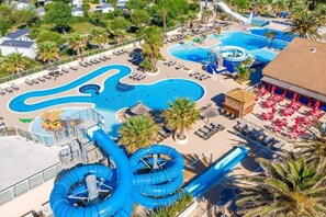 Une grande piscine extérieure dotée de plusieurs toboggans et d’attractions aquatiques, entourée de chaises longues et de parasols.
