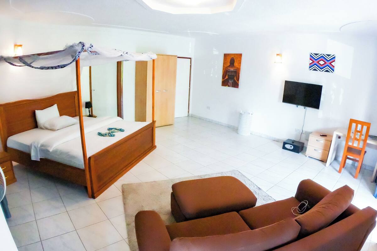 A bedroom with a four-poster bed, a sofa, a TV, and a small desk.
