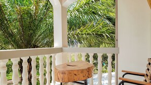 Un balcon agrémenté d’une table et d’une chaise en bois, entouré de balustrades blanches et d’un feuillage verdoyant et luxuriant.