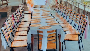 Une longue table, recouverte de sets de table en fibres tressées, est entourée de chaises en bois.