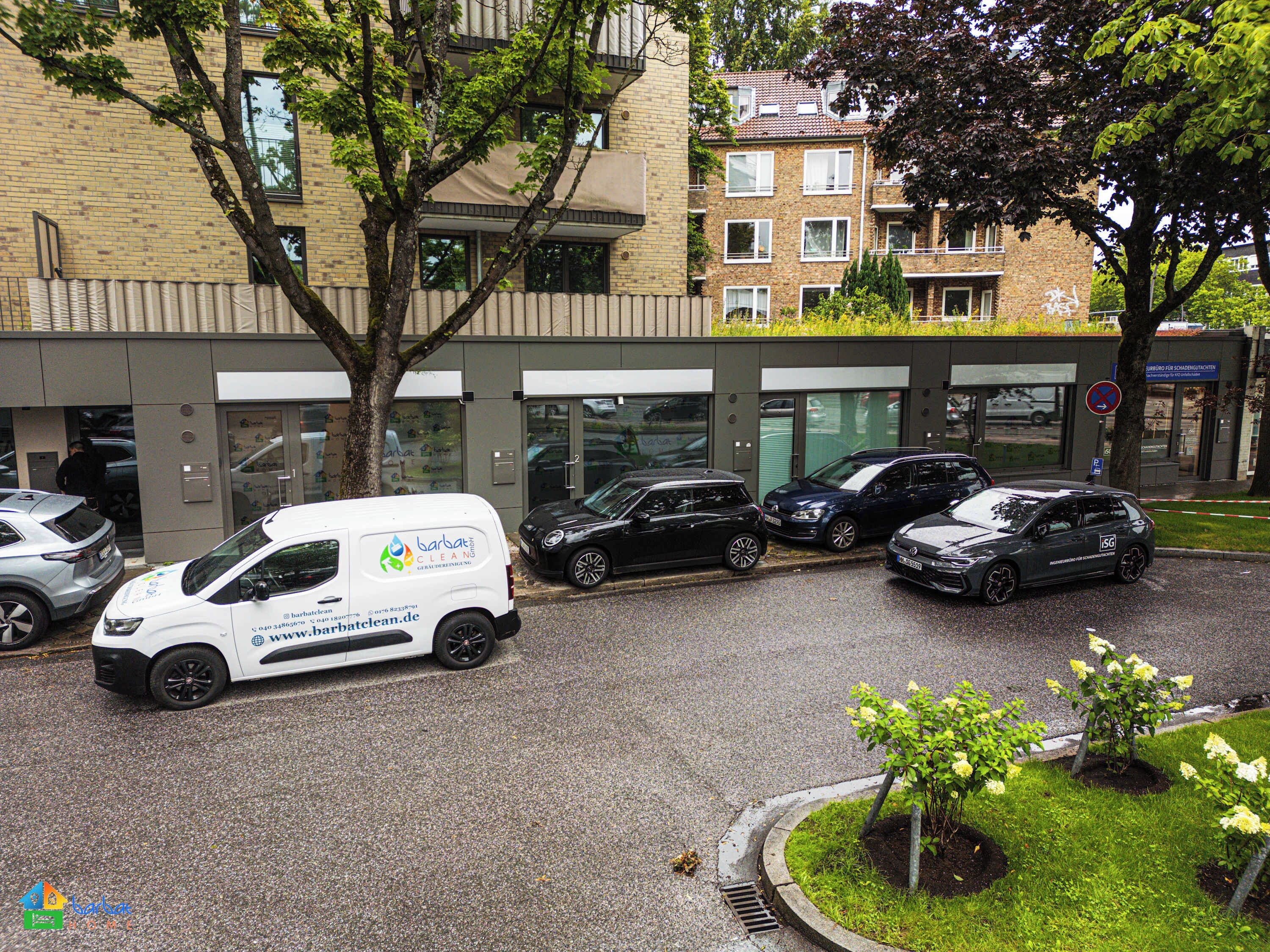 Un edificio con una facciata moderna, auto parcheggiate e un albero di fronte.