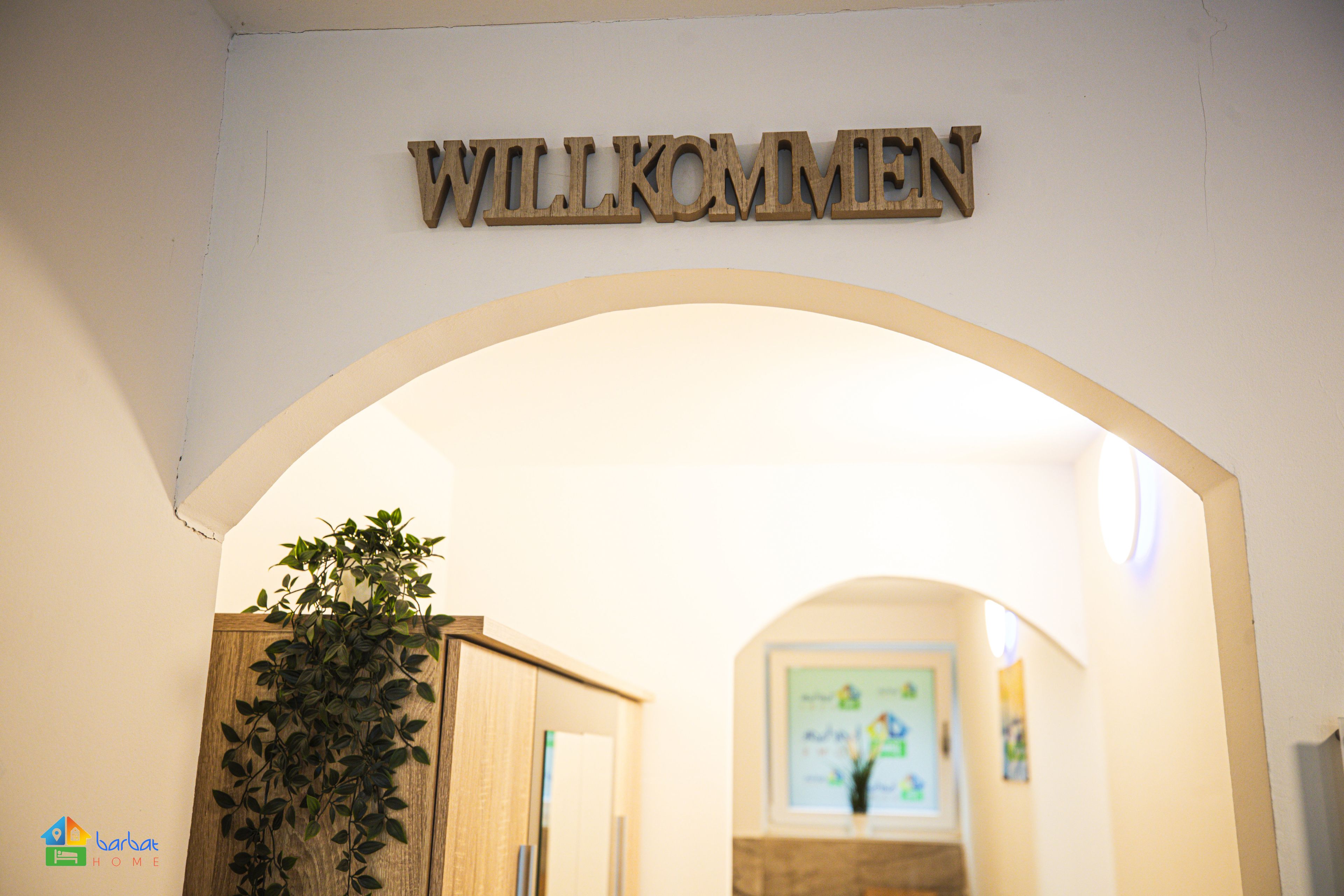 Une enseigne en bois portant le mot « WILLKOMMEN » au-dessus d’une porte en arc de cercle.
