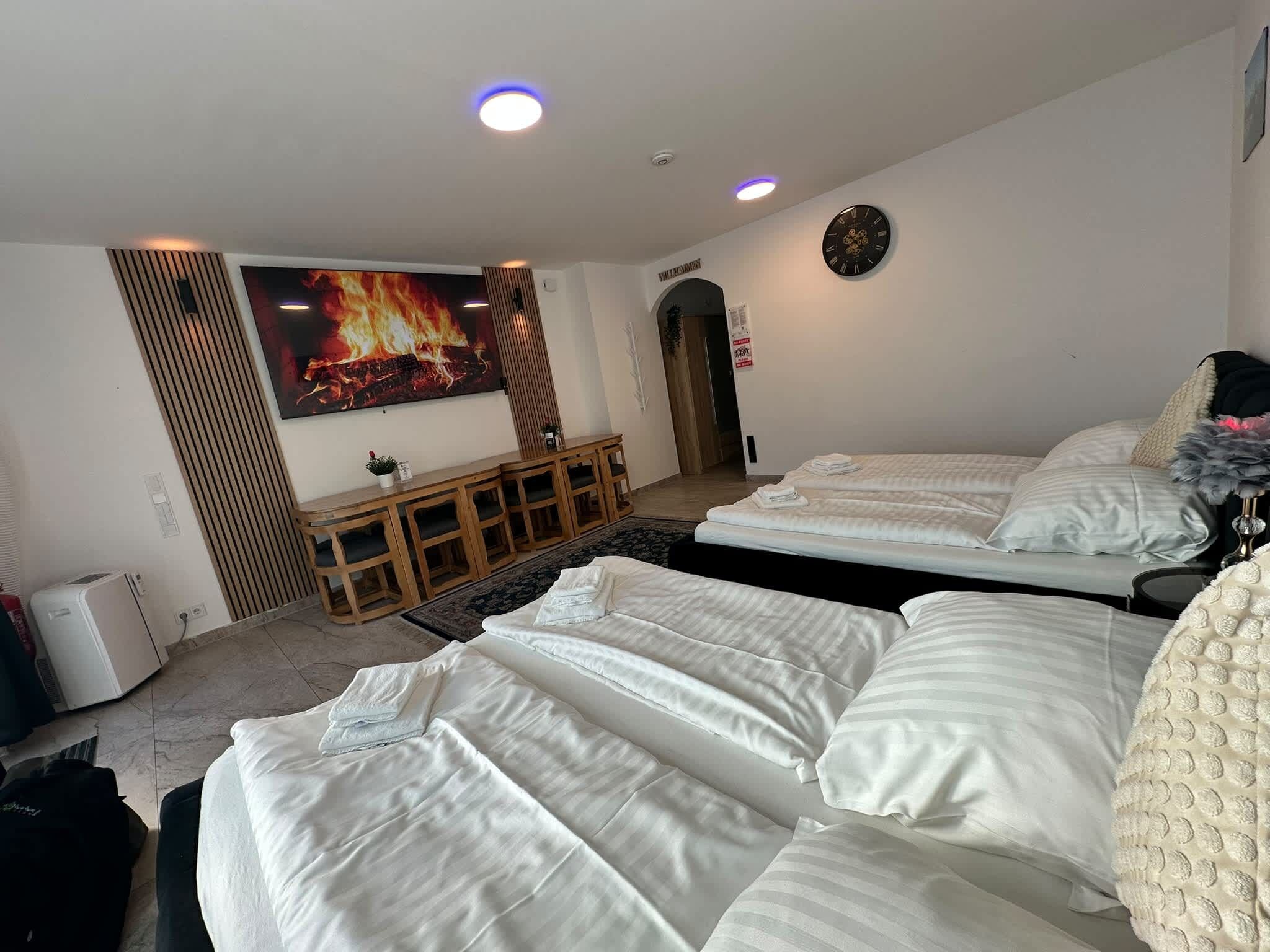 A hotel room with two beds, a TV, a clock, and a fireplace.