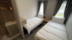 Un dormitorio con dos camas individuales, una mesita de noche, un armario y una ventana con cortinas.