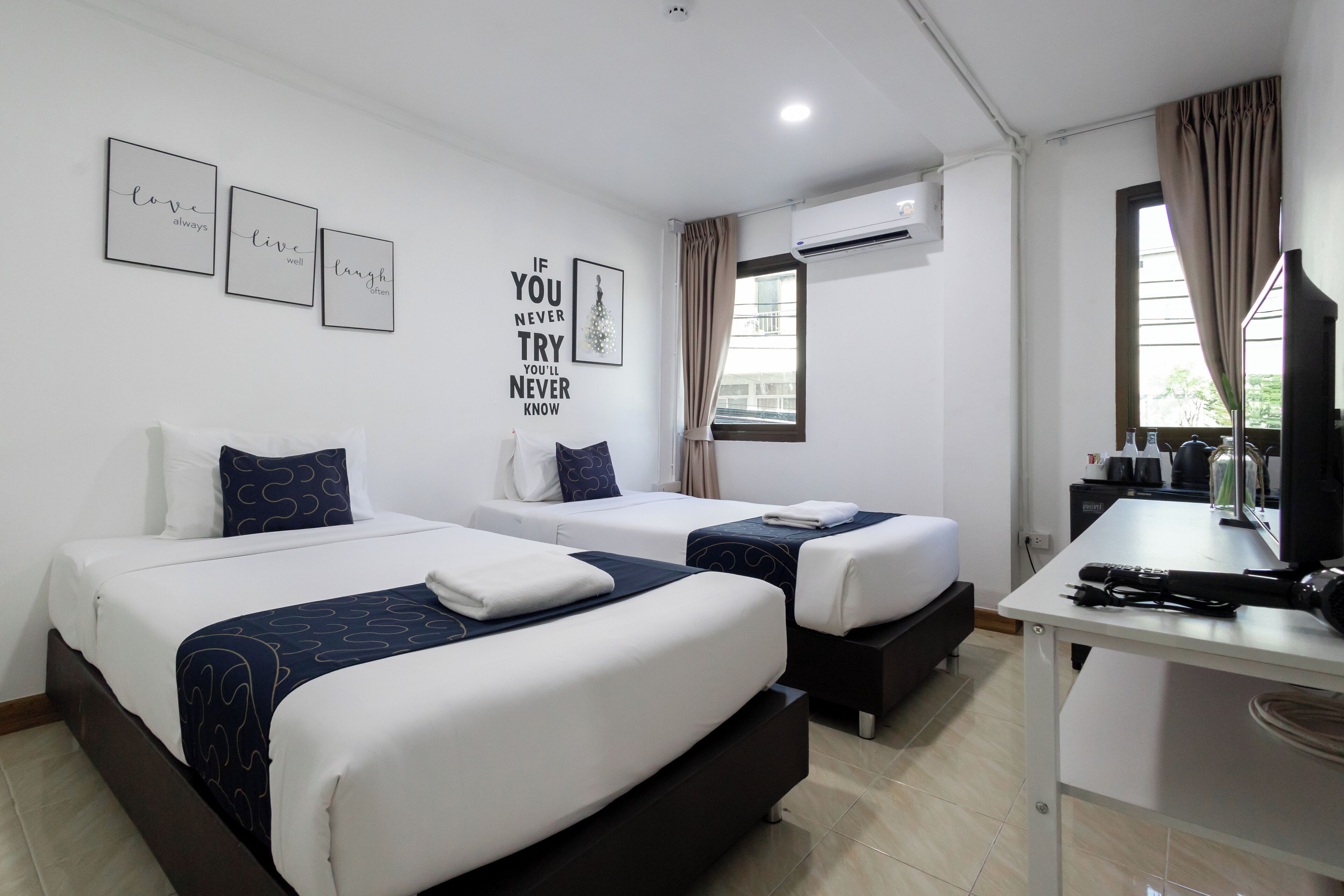 A hotel room with two beds, a desk, and an air conditioning unit.